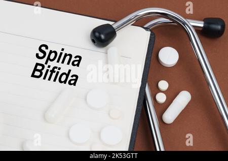 Medical concept. On a brown surface lies a stethoscope, pills and a notepad with the inscription - Spina Bifida Stock Photo