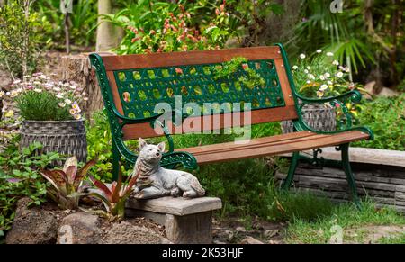 Decorative wrought iron and timber bench surrounded by lush garden with flowers, in Australia Stock Photo