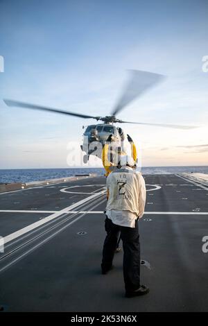 PHILIPPINE SEA (Sept. 23, 2022) – Boatswain’s Mate 2nd Class Christopher Treanor, from Mapleton, Minnesota, signals an MH-60R Sea Hawk helicopter assigned to Helicopter Maritime Strike Squadron (HSM) 35 aboard the guided-missile destroyer USS Zumwalt (DDG 1000) while operating in the Philippine Sea, Sept. 23. Zumwalt is conducting underway operations in support of a free and open Indo-Pacific. (U.S. Navy photo by Mass Communication Specialist 2nd Class Jaimar Carson Bondurant) Stock Photo