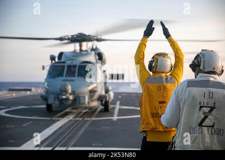 PHILIPPINE SEA (Sept. 23, 2022) – Boatswain’s Mate 2nd Class Christopher Treanor, from Mapleton, Minnesota, signals an MH-60R Sea Hawk helicopter assigned to Helicopter Maritime Strike Squadron (HSM) 35 aboard the guided-missile destroyer USS Zumwalt (DDG 1000) while operating in the Philippine Sea, Sept. 23. Zumwalt is conducting underway operations in support of a free and open Indo-Pacific. (U.S. Navy photo by Mass Communication Specialist 2nd Class Jaimar Carson Bondurant) Stock Photo