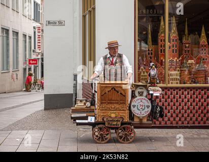 Germany, Lubeck - July 13, 2022: Older man is Organ grinder with small street organ on wheels, standing in Breite street. Stock Photo