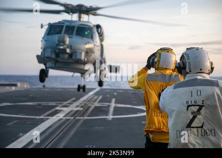 PHILIPPINE SEA (Sept. 23, 2022) – Boatswain’s Mate 2nd Class Christopher Treanor, from Mapleton, Minnesota, signals an MH-60R Sea Hawk helicopter assigned to Helicopter Maritime Strike Squadron (HSM) 35 aboard the guided-missile destroyer USS Zumwalt (DDG 1000) while operating in the Philippine Sea, Sept. 23. Zumwalt is conducting underway operations in support of a free and open Indo-Pacific. (U.S. Navy photo by Mass Communication Specialist 2nd Class Jaimar Carson Bondurant) Stock Photo