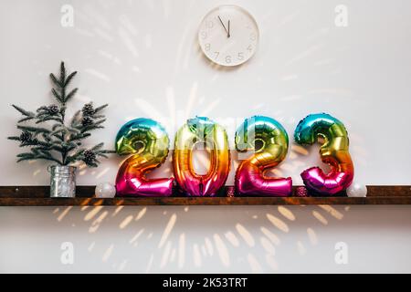 Christmas tree, white clock at 12 and decorations in front of white wall with fireworks projection. Interior Stock Photo