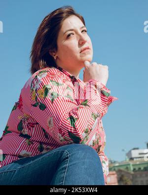 beautiful young Caucasian woman of Argentine ethnicity and plus size, posing crouched with a thoughtful face and a hand on her chin, vertical image fo Stock Photo