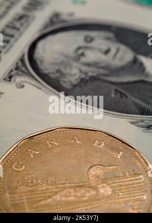 Canadian one dollar coin on top of US one dollar bill. Stock Photo