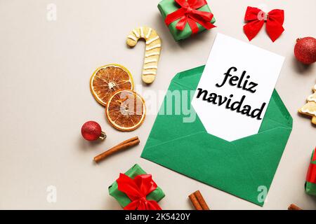 Card with text FELIZ NAVIDAD (Spanish for Merry Christmas) in envelope, gifts, food and decor on light background Stock Photo