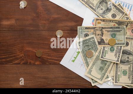 Dollar banknotes with coins and diagrams on dark wooden background. Exchange rate concept Stock Photo