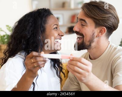 Young multi-ethnic couple happily looking at a pregnancy test. Celebrating pregnancy Stock Photo