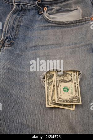 US dollars slipping through hole on front pocket of pair of blue jeans. Stock Photo
