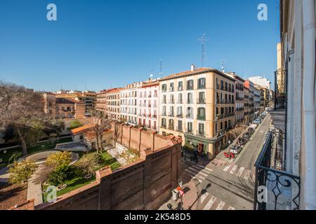 Facades of old residential buildings at a crossroads with cobbled paths, balconies and a large wall of a monastery with a large park inside Stock Photo