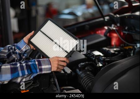 Caucasian female auto mechanic changes the engine air filter in the car. Stock Photo