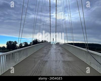 Vanishing perspective of suspension bridge with cloudy sky above Stock Photo