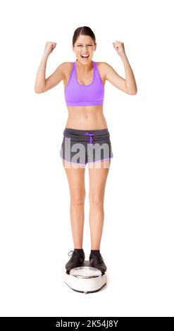 Celebrating her achievements. Full length shot of an ecstatic young woman weighing herself on a scale isolated on white. Stock Photo