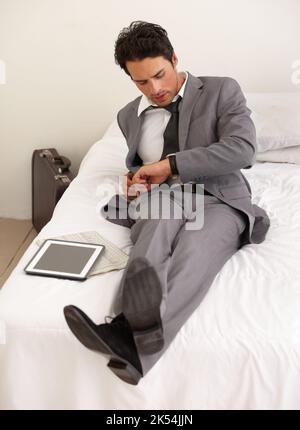 I fell asleep...A handsome young businessman lying on his bed with his digital tablet and looking at his watch. Stock Photo