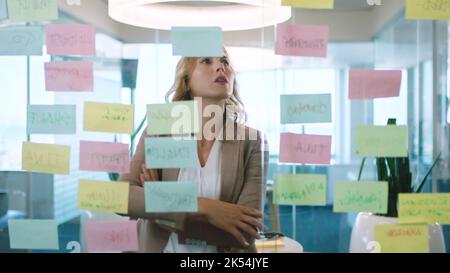 Sticky note, reading and business woman planning strategy for marketing idea on glass in an office at work. Employee working in project management Stock Photo