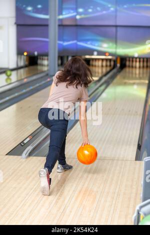 A woman throws a ball into a bowling alley. Paths with balls and pins for bowling. A fun game for the company. Stock Photo