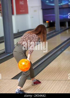 A woman throws a ball into a bowling alley. Paths with balls and pins for bowling. A fun game for the company. Stock Photo