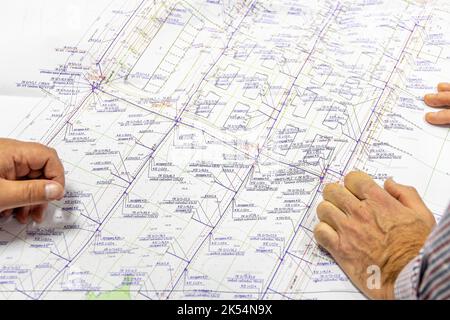 Men's hands lie on project of future engineering gas supply systems for cottage settlement in private sector. Brainstorming in progress. Stock Photo