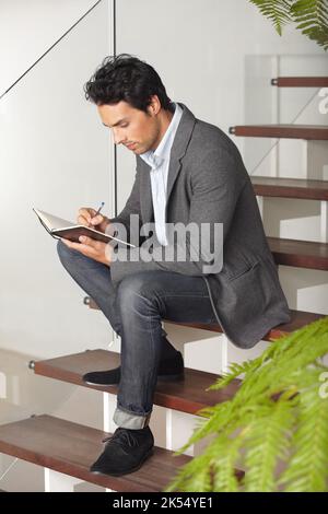 Making appointments. A young businessman sitting on a staircase writing in his journal. Stock Photo