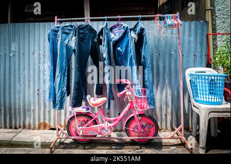 A pink kids bicycle stands by a clothes line in the tight streets and lanes of the Ruamrudee area near to Lumpini Park Bangkok Thailand. Stock Photo