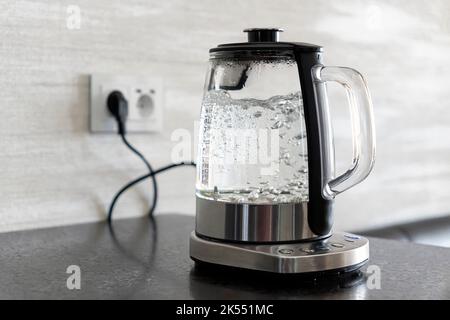 Transparent electric kettle with boiling water on table in the kitchen Stock Photo
