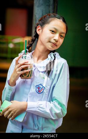 A beautiful Thai school girl poses and laughs holding her Starbucks