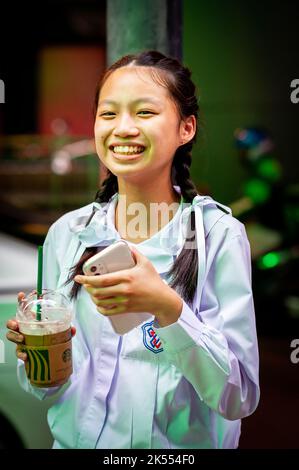 A beautiful Thai school girl poses and laughs holding her Starbucks