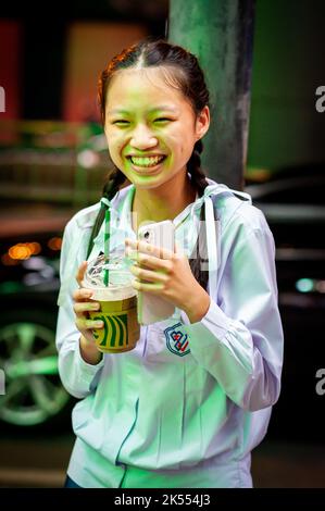 A beautiful Thai school girl poses and laughs holding her Starbucks