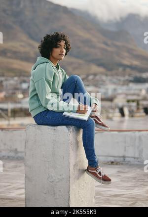 Art, city and a woman drawing in notebook sitting on rooftop looking for inspiration and creativity from cityscape. Creative girl from India on roof Stock Photo