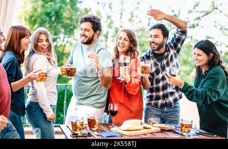 Happy friends having fun eating at house balcony dinner party - Young people drinking beer and wine at fancy alternative roof top venue together - Din Stock Photo