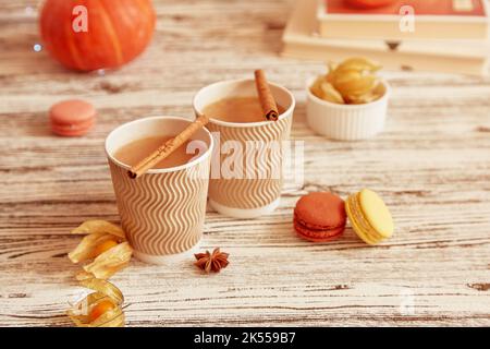 Aesthetics lagom lunch - cardboard cups of pumpkin latte and cinnamon sticks. Autumn coffee time with macaroons. Cozy atmospheric home. Stock Photo