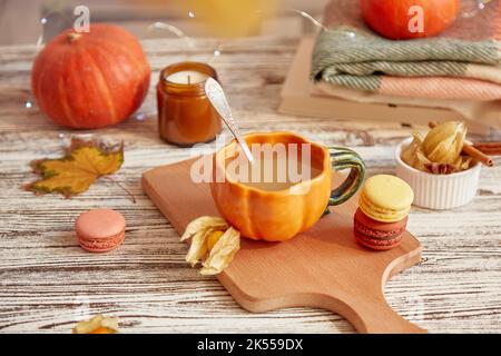 Aesthetics seasonal pumpkin latte in cup shape of pumpkin. Lagom lifestyle, colorful pumpkins, macaroons and leaves. Cozy autumn home. Stock Photo