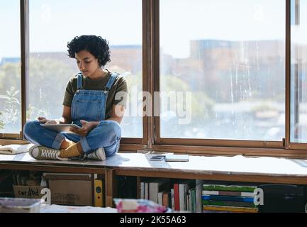 Tablet, creative woman and on table and at window using digital device for social media apps, texting and chatting during break. Girl artist or female Stock Photo