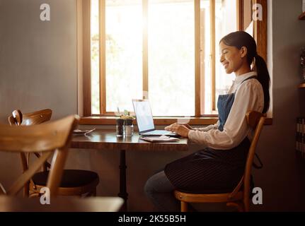 Female, coffee shop owner and laptop restaurant worker on a work break on a laptop. Happy smile of waiter employee online at a cafe using technology Stock Photo