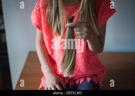 Girl holding her long cut off natural blond ponytail hair tied together. Stock Photo