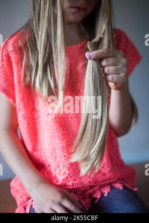 Girl holding her long cut off natural blond ponytail hair tied together. Stock Photo