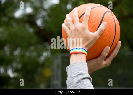 Cropped photo of male hands holding a basketball ball wearing a rainbow bracelet Stock Photo