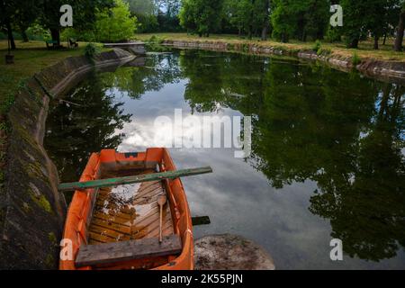 Picture of an abandoned garden park in Europe, with an abandoned pond, fully of water,with a half sunken rowing boat. Stock Photo