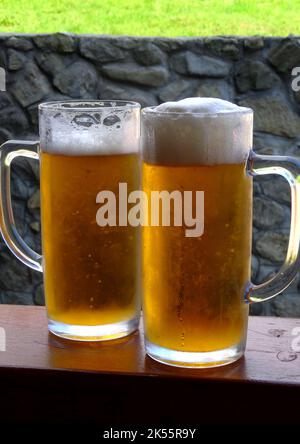 Tall half-liter glasses of light chilled beer with cool foam on a wooden desk at outdoor pub Stock Photo