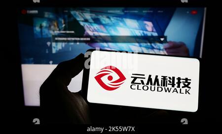 Person holding cellphone with logo of Chinese company CloudWalk Technology Co. Ltd. on screen in front of webpage. Focus on phone display. Stock Photo