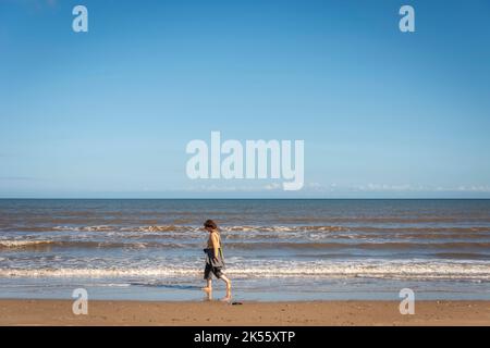 Middle aged woman walking along the tide line at Fraisthorpe Beach, Bridlington, East Yorkshire, UK Stock Photo