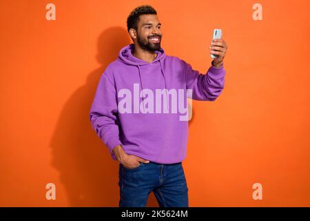 Photo of handsome man boy wear violet pullover use modern device speak video make post for followers isolated on orange color background Stock Photo