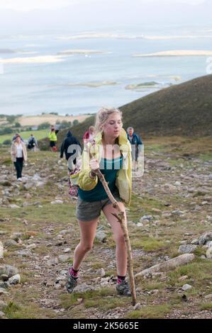 A young lady uses a stick to help her climb Croagh Patrick on Reek Sunday, when Roman Catholic pilgrims climb to the top to follow the steps of Saint Patrick. Stock Photo