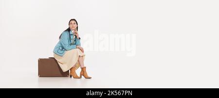 Stylish young woman sitting on vintage suitcase with deay look isolated over white background. Travelling Stock Photo