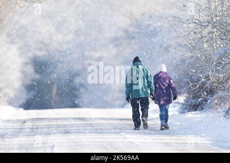 Rear view of a married couple isolated outdoors in winter walking down an empty, snow-covered, country road while it is snowing. Stock Photo