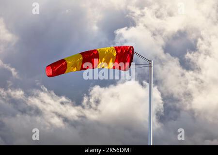 Yellow and red striped windsock or wind cone against dark cloudy sky, indicating wind direction and force. Copy space for your text. Stock Photo