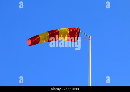 Yellow and red striped windsock or wind cone against clear blue sky, indicating wind direction and force. Copy space for your text. Stock Photo