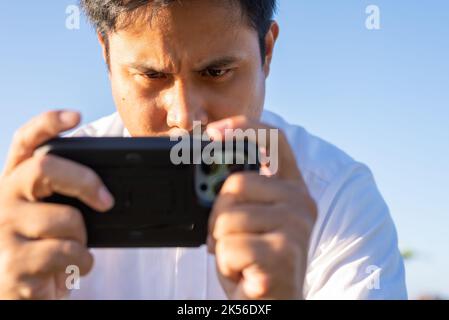 An Asian Filipino man is focusing on playing mobile games on his smartphone. Stock Photo