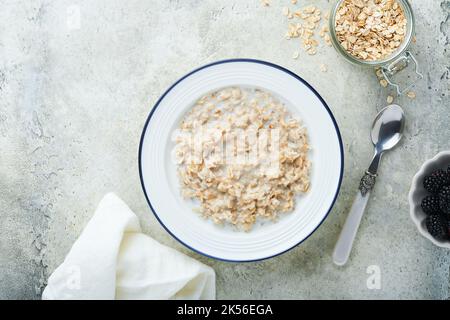 Oatmeal. Bowl of oatmeal porridge with strawberry, almond and milk on vintage light grey teal table. Top view in flat lay style. Natural ingredients. Stock Photo