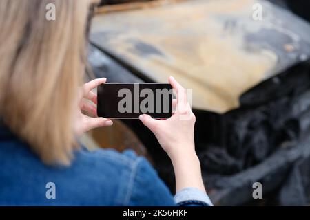 Insurance agent woman photographs burned-out car on smartphone Stock Photo